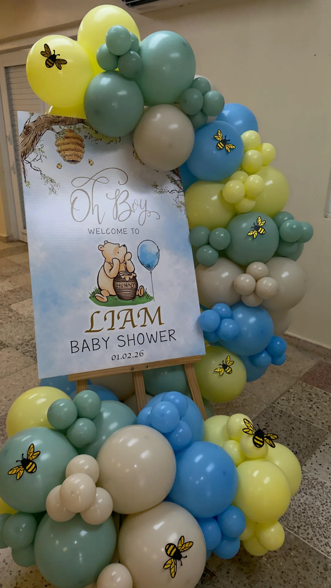 Baby shower con globos azules verdes y amarillos, abejas y cartel de bienvenida